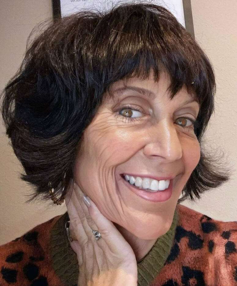 Ältere Frau mit einem peppigen schwarzen Bob-Haarschnitt lächelt fröhlich.